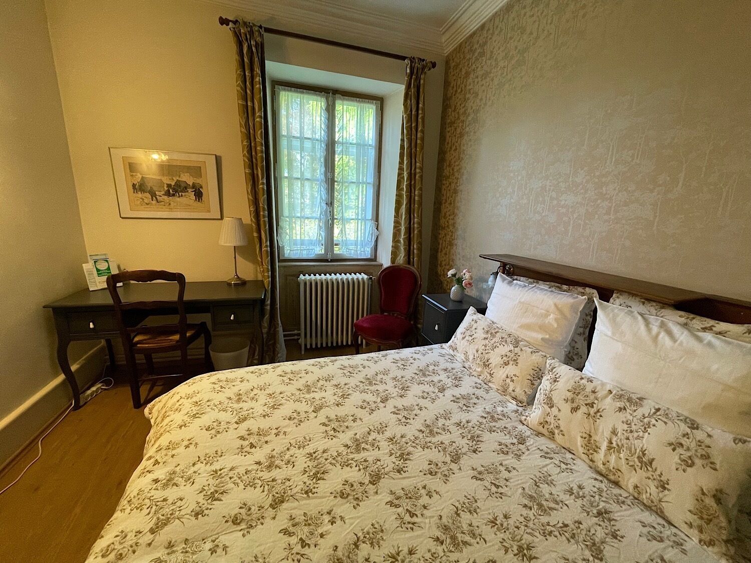 A bedroom with a bed, a desk, a chair, a radiator, and a window with curtains.