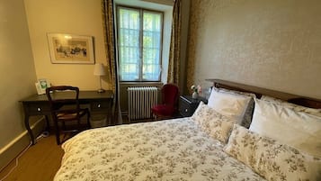 A bedroom with a bed, a desk, a chair, a radiator, and a window with curtains.