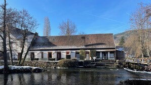 Un bâtiment traditionnel avec un toit en tuiles, un mur en pierre et un petit étang à l’avant.