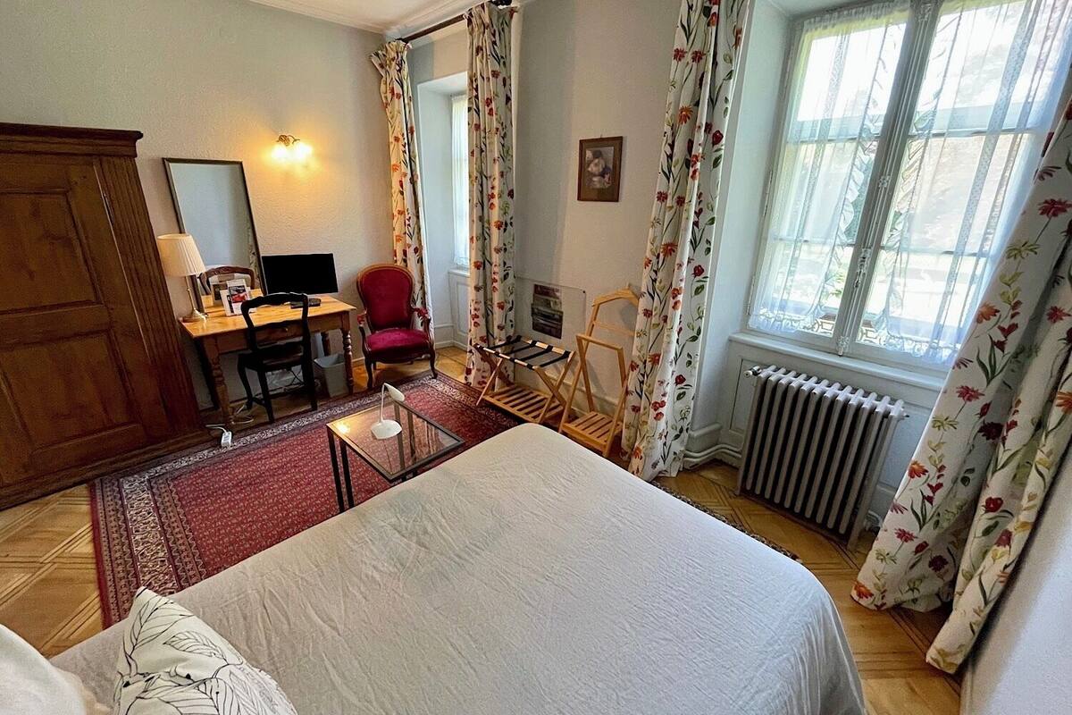 Ein Hotelzimmer mit einem Bett, einem Schreibtisch mit Computer, einem Sessel, einem Heizkörper und Vorhängen.