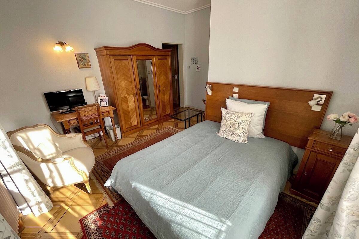 Ein Schlafzimmer mit einem gro ßen Bett, einem Holzschrank, einem Schreibtisch mit Stuhl, einem Fernseher und einem kleinen Tisch mit einer Vase.