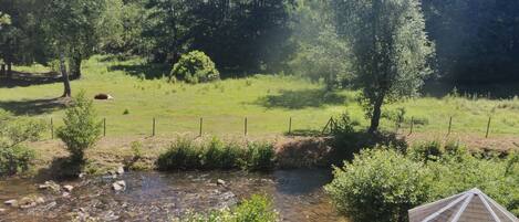 A rural landscape with a small white gazebo, a stream, and a forested hill in the background.