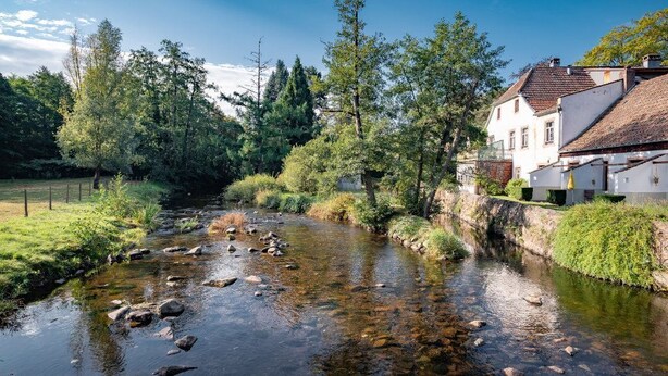 Une rivière traverse une zone rurale, et un bâtiment blanc se trouve sur la rive droite.