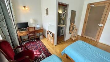 A hotel room with two single beds, a desk with a computer, a chair, a red armchair, a mirror, and a bathroom visible through an open door.