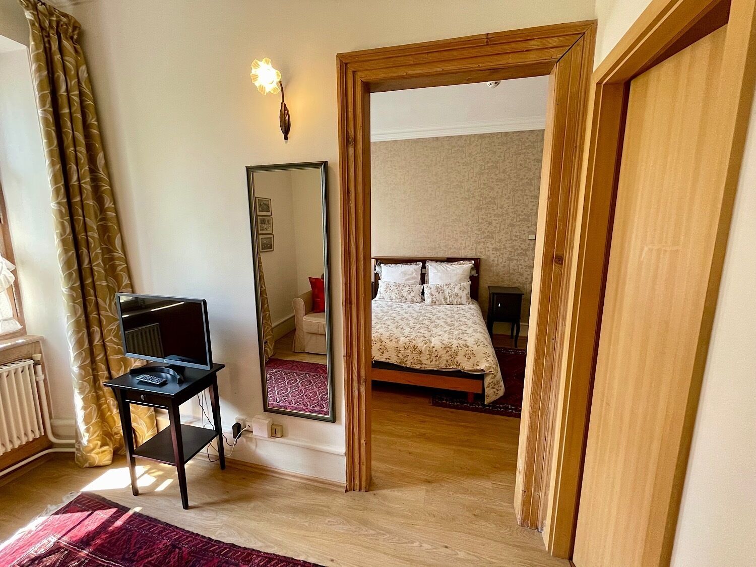 Un dormitorio con cama, escritorio con computadora, espejo y ventana con cortinas.