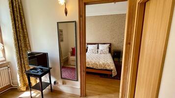 Un dormitorio con cama, escritorio con computadora, espejo y ventana con cortinas.