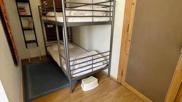 Habitación con literas, suelo de madera, un taburete pequeño y una puerta.