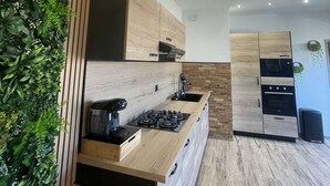 A modern kitchen with wooden cabinetry, a built-in stove, and pendant lights. - Gîte nature M&J (Calais)
