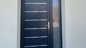 A black door with horizontal slats and a metal handle. Above the door, there is a sign with the text "Gite Nature" and a logo. - Gîte nature M&J (Calais)