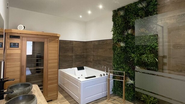 A modern bathroom with a wooden vanity, a large bathtub, and a green wall with plants. - Gîte nature M&J (Calais)
