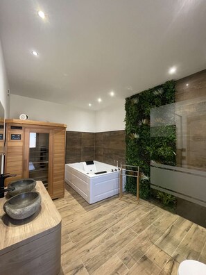 A modern bathroom with a wooden vanity, a large bathtub, and a green wall with plants. - Gîte nature M&J (Calais)