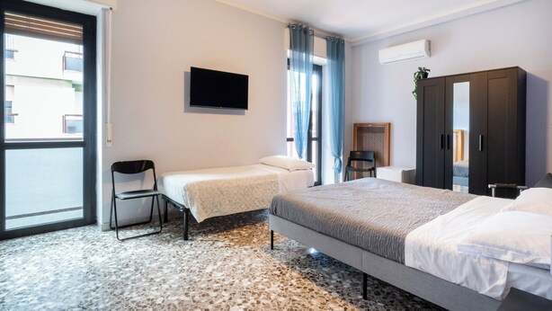 A hotel room with a bed, a chair, a TV, a wardrobe, and a window with curtains. - Appartamento Matthias by Wonderful Italy (Bari)