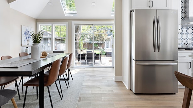 A modern kitchen with a stainless steel refrigerator, a dining area with a long table and chairs, and a view of the backyard through large sliding glass doors. - Cute and Quaint on Carrollton | Patio & Game Room (Indianapolis)