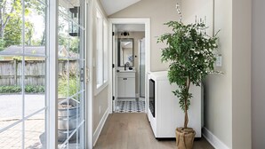 A hallway with a glass door leading outside, a potted plant, a white refrigerator, and a tiled floor. - Cute and Quaint on Carrollton | Patio & Game Room (Indianapolis)