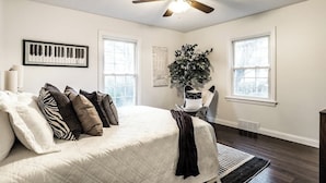 A bedroom with a bed, a ceiling fan, a window, and a plant. - The Crestview Bungalow | Steps to Broad Ripple! (Indianapolis)