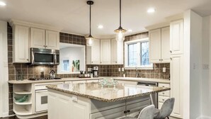 A modern kitchen with white cabinets, a granite island, and pendant lighting. - The Crestview Bungalow | Steps to Broad Ripple! (Indianapolis)