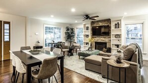 A spacious living room with a fireplace, a dining area, and a seating area with a sofa and chairs. - The Crestview Bungalow | Steps to Broad Ripple! (Indianapolis)