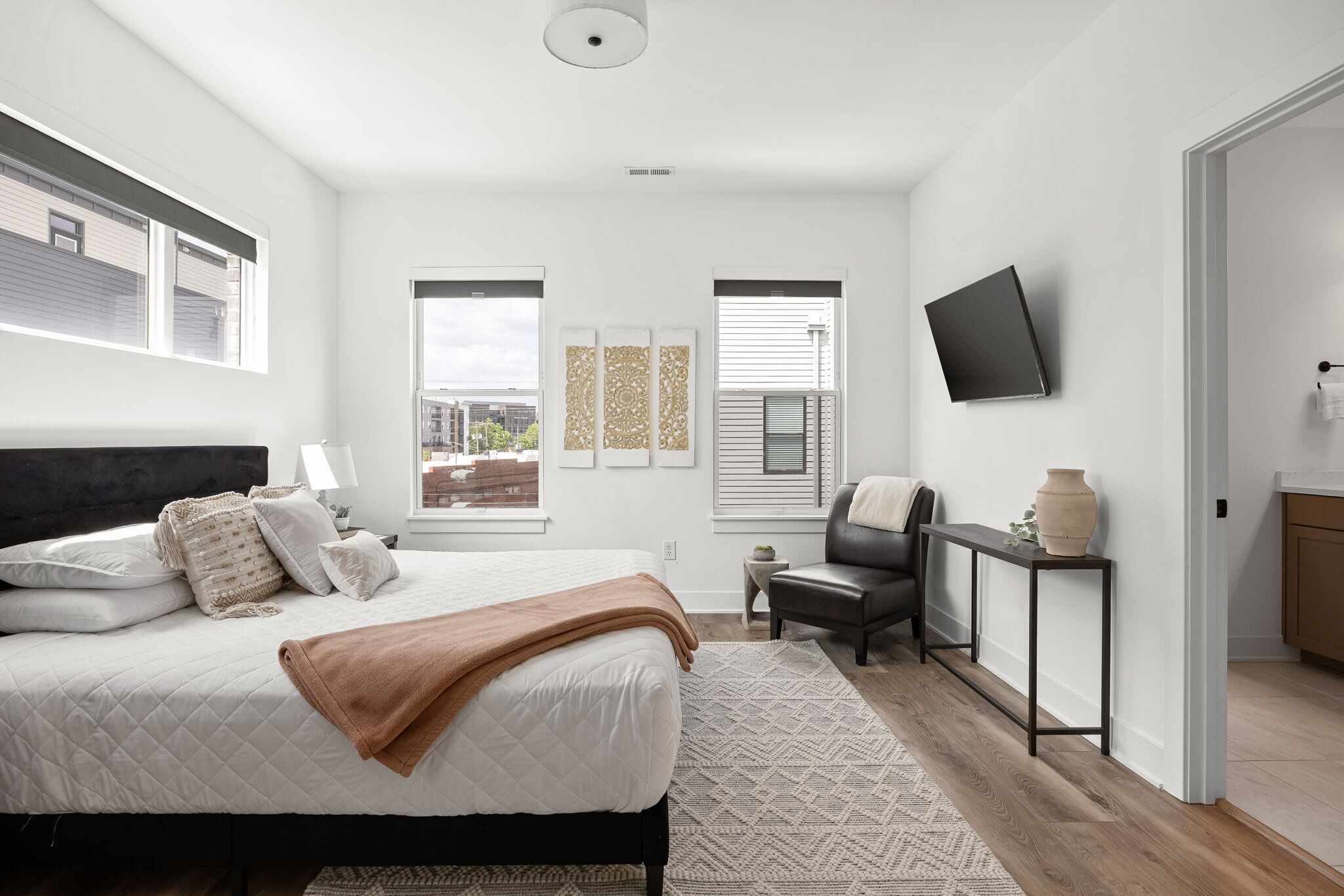 A modern bedroom with a bed, bedside table, chair, TV, and artwork on the wall.