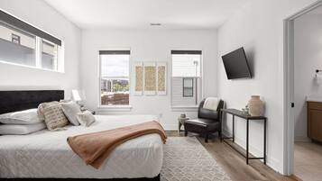 A modern bedroom with a bed, bedside table, chair, TV, and artwork on the wall.