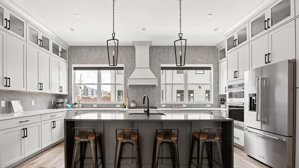 A modern kitchen with a large island, bar stools, stainless steel appliances, and a view of the city.