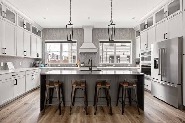 A modern kitchen with a large island, bar stools, stainless steel appliances, and a view of the city.