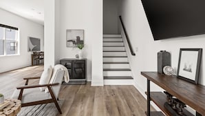 A modern interior with a staircase, a wooden floor, a seating area with a chair, a small table, and a wall-mounted TV.