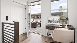 A room with a desk, a chair, a window, a door, and a view of an outdoor patio with furniture.