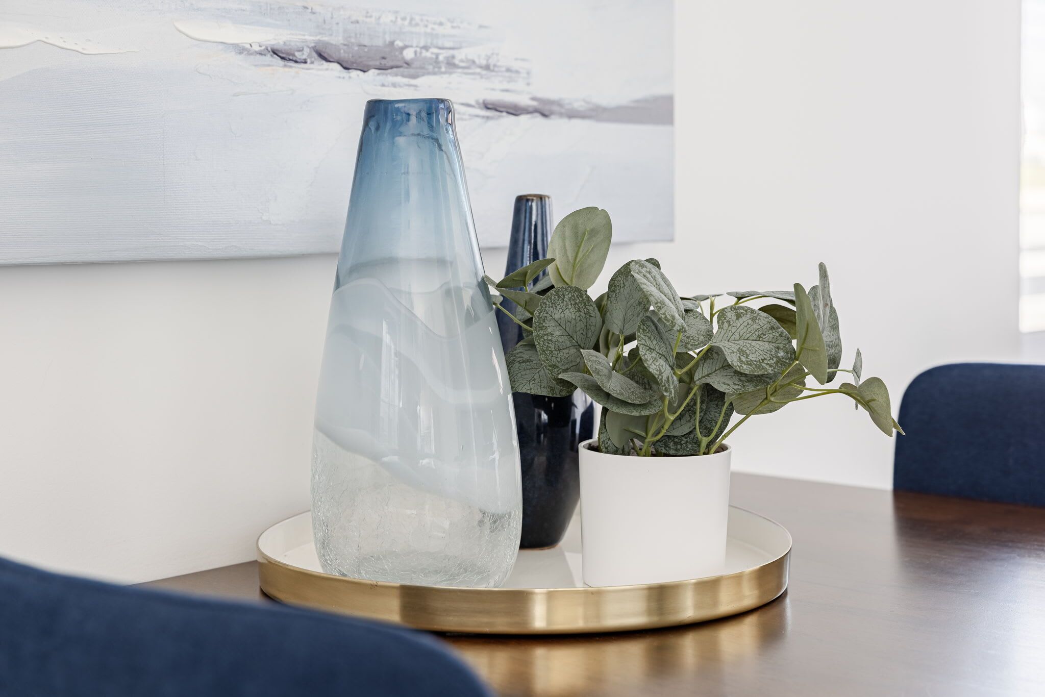 Une pièce avec une table ronde, un vase bleu, un vase noir et une plante en pot.