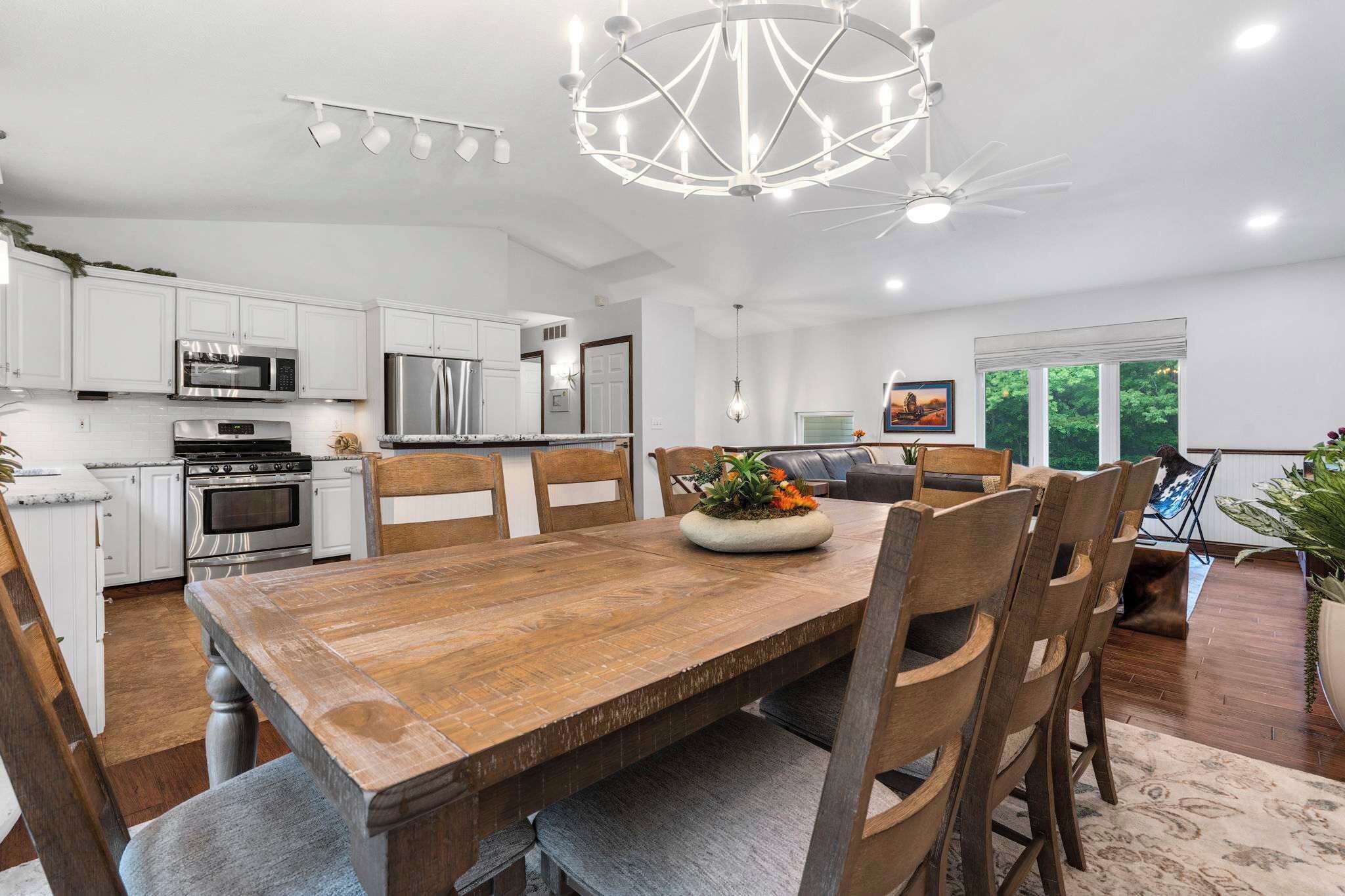 A modern kitchen with white cabinetry, stainless steel appliances, and a wooden dining table with chairs.