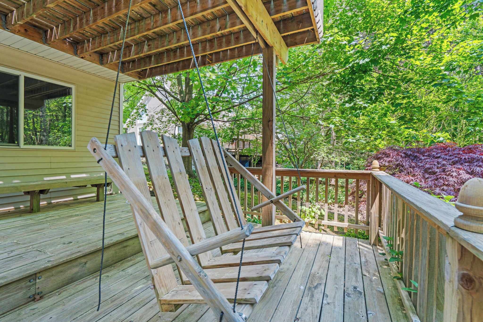 Une terrasse en bois avec une chaise suspendue et une rambarde en bois.