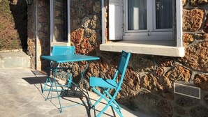 Un edificio in pietra con una finestra e un piccolo spazio esterno arredato con sedie blu e un tavolo.