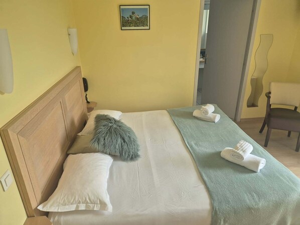 Un lit bien fait, avec un oreiller moelleux, une serviette verte et deux serviettes roulées posées sur une couvre-lit de couleur claire.