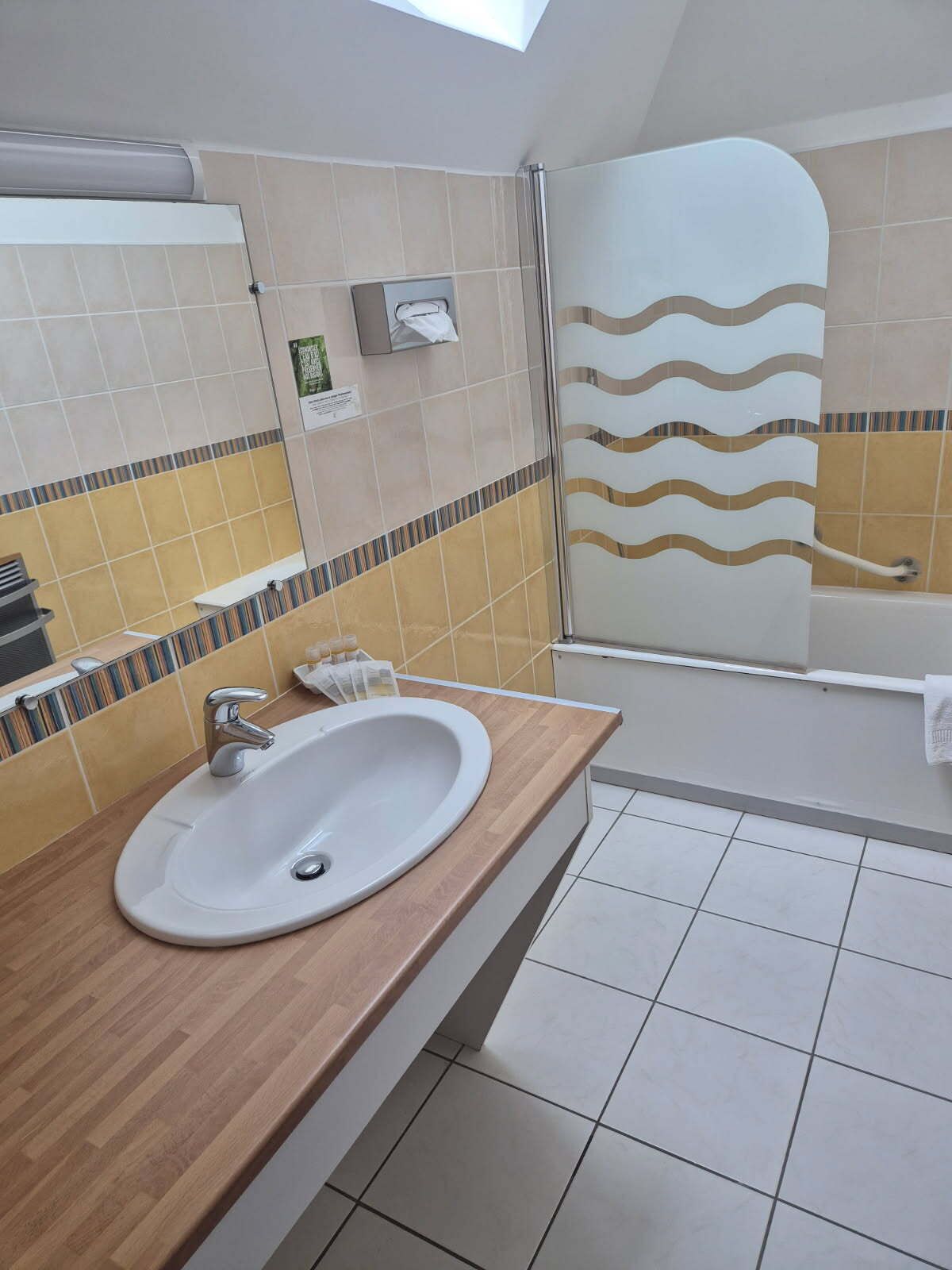 A bathroom with a sink, mirror, shower, and tiled walls.
