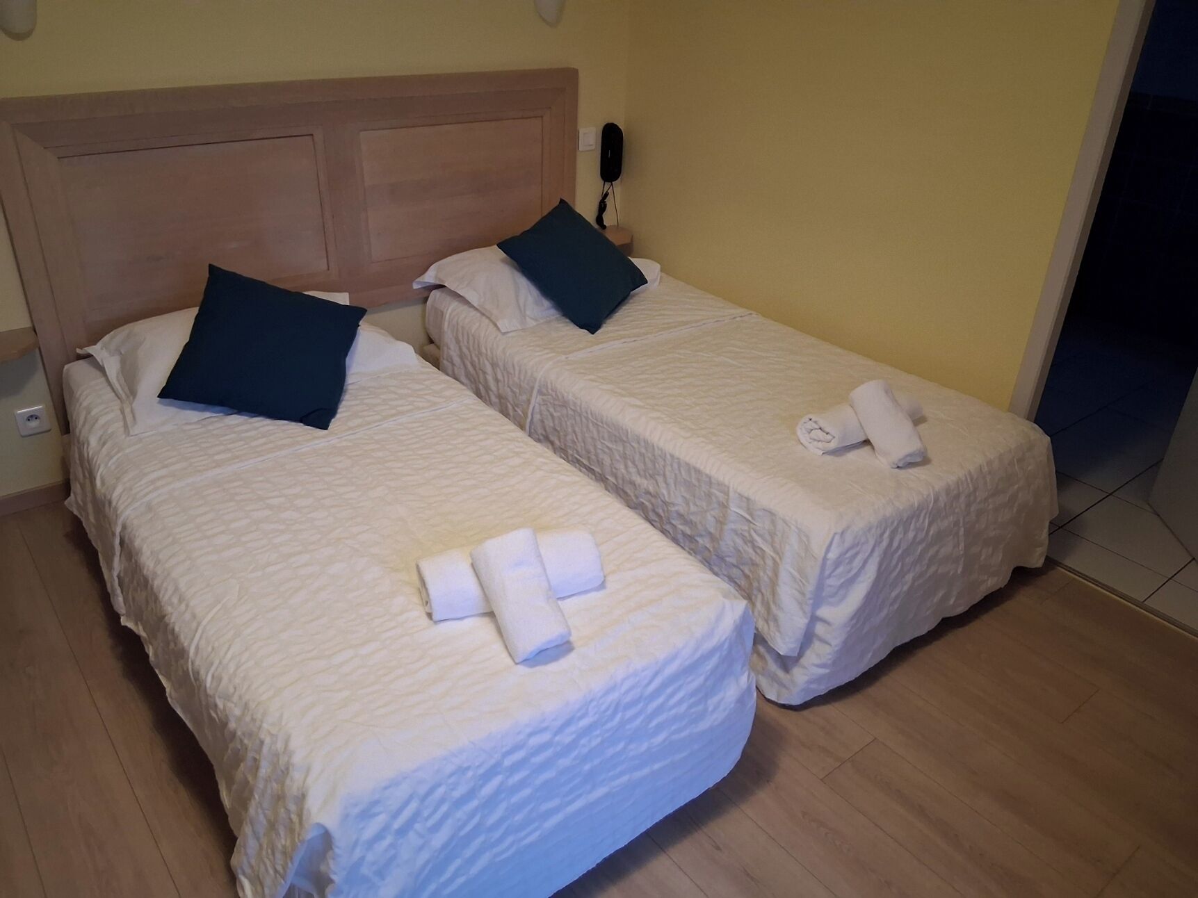 Deux lits simples avec des têtes de lit, du linge de lit blanc et un téléphone sur la table de chevet.