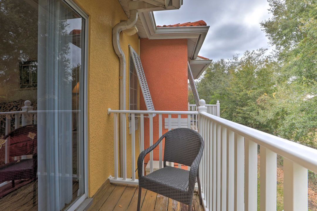 A balcony with a chair, a white railing, and a view of trees.