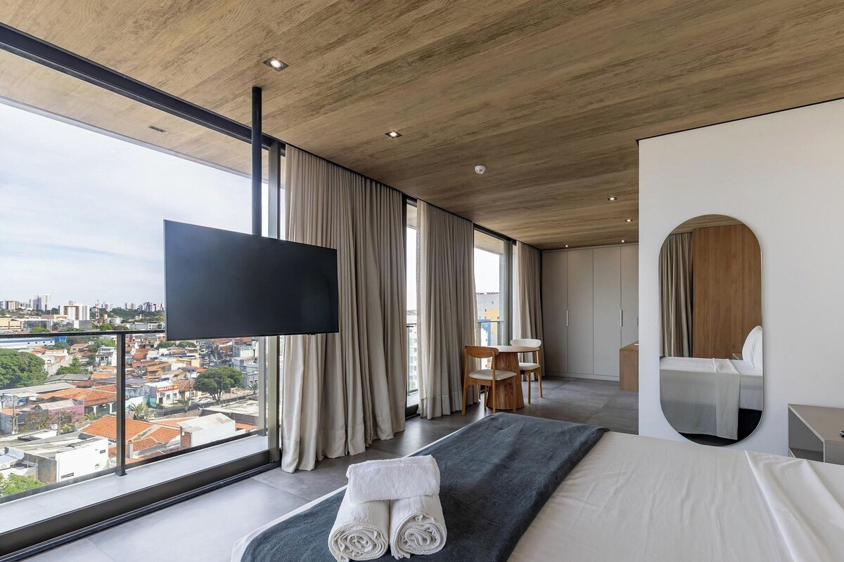 Een moderne hotelkamer met een groot bed, een flatscreen televisie, uitzicht op de stad en een zithoek.
