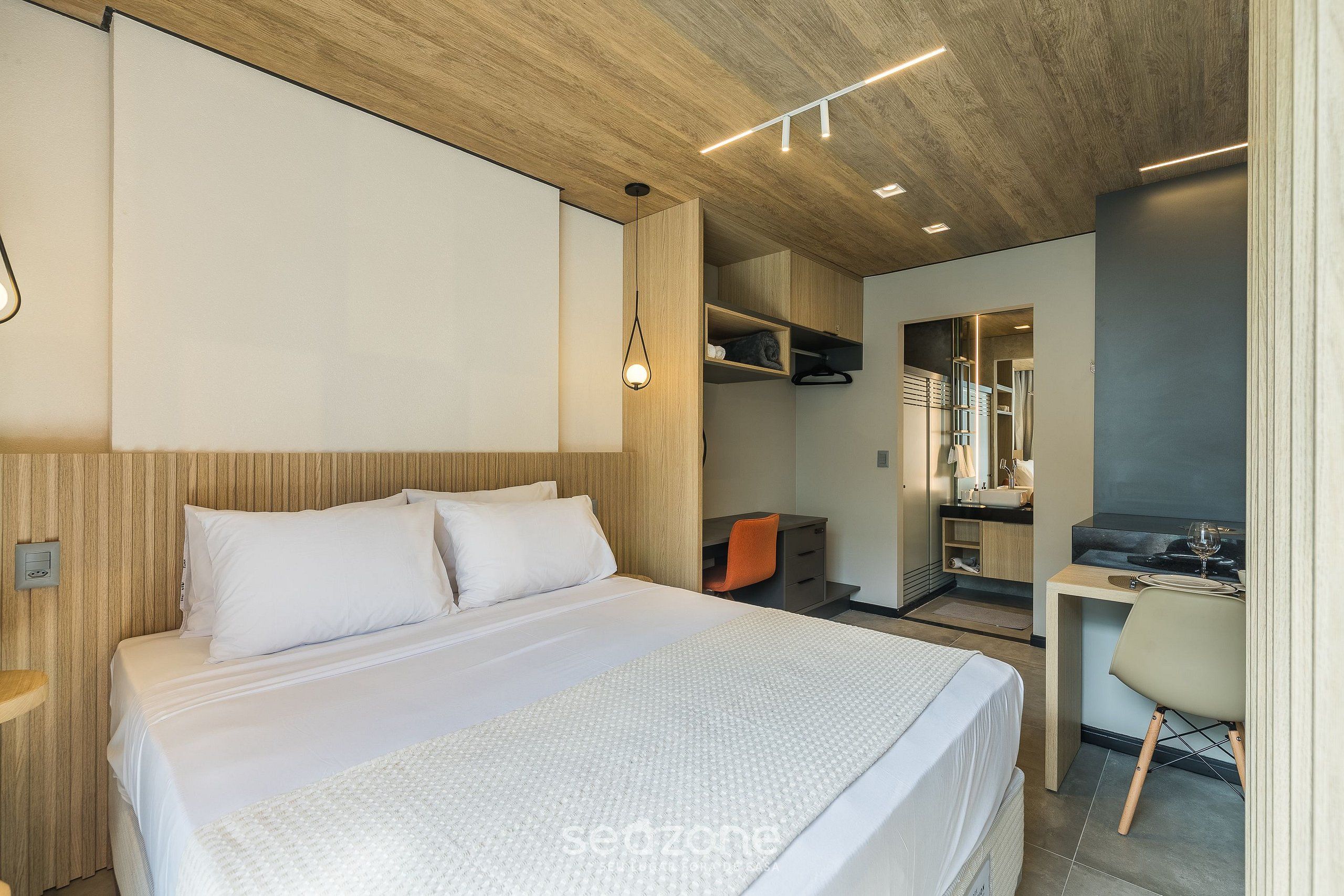 Una habitación de hotel moderna con cama, escritorio, silla, paneles de madera y estanterías empotradas.