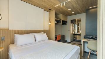Una habitación de hotel moderna con cama, escritorio, silla, paneles de madera y estanterías empotradas.