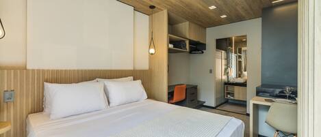 Una habitación de hotel moderna con cama, escritorio, silla, paneles de madera y estanterías empotradas.