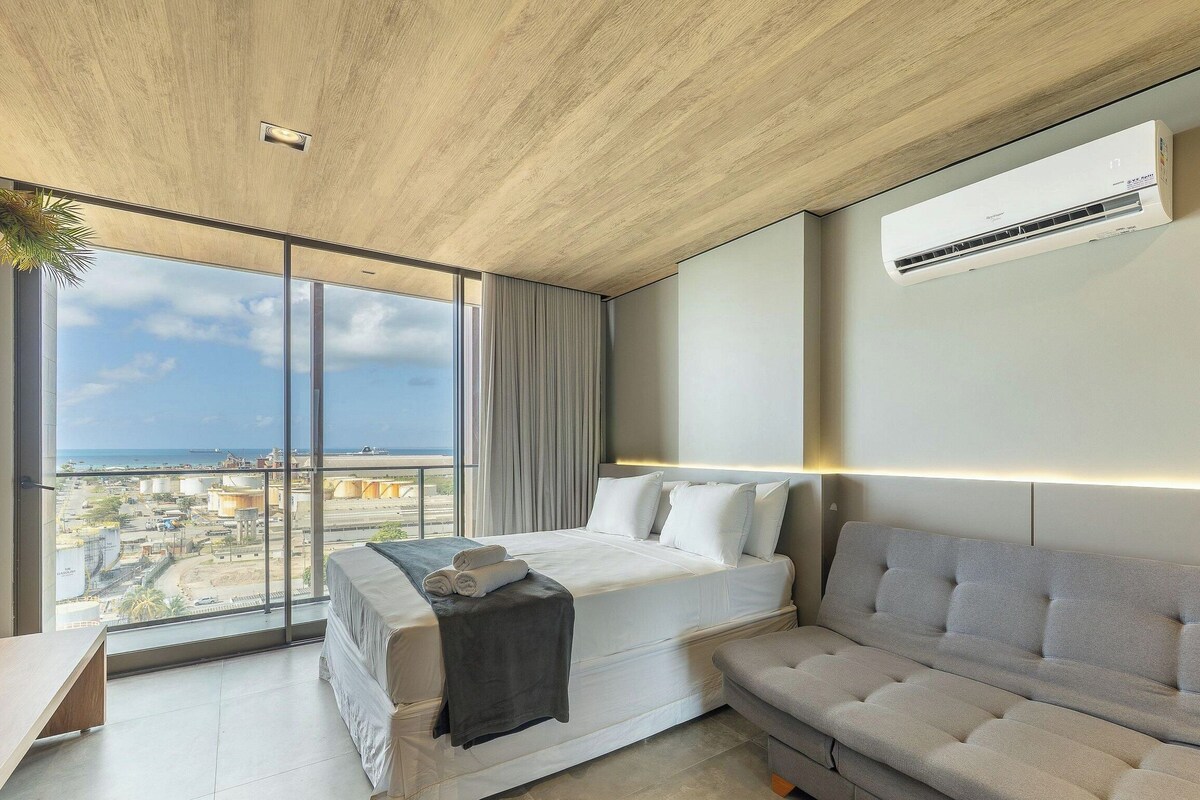 Een moderne hotelkamer met een groot raam, een bed, een slaapbank en een airconditioning.
