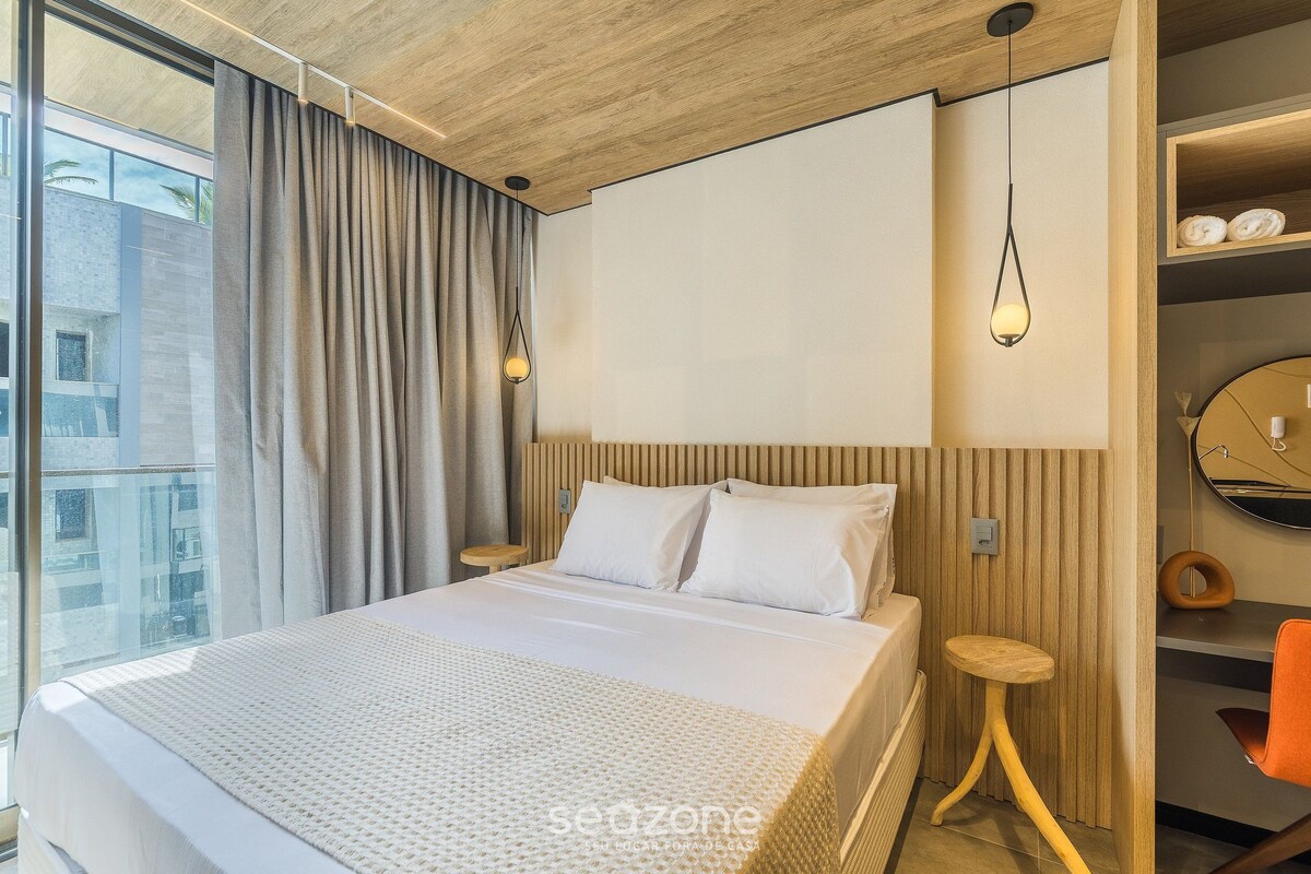 Een moderne hotelkamer met een groot bed, een houten hoofdeinde, een klein houten krukje, een ronde spiegel en uitzicht op de stad.