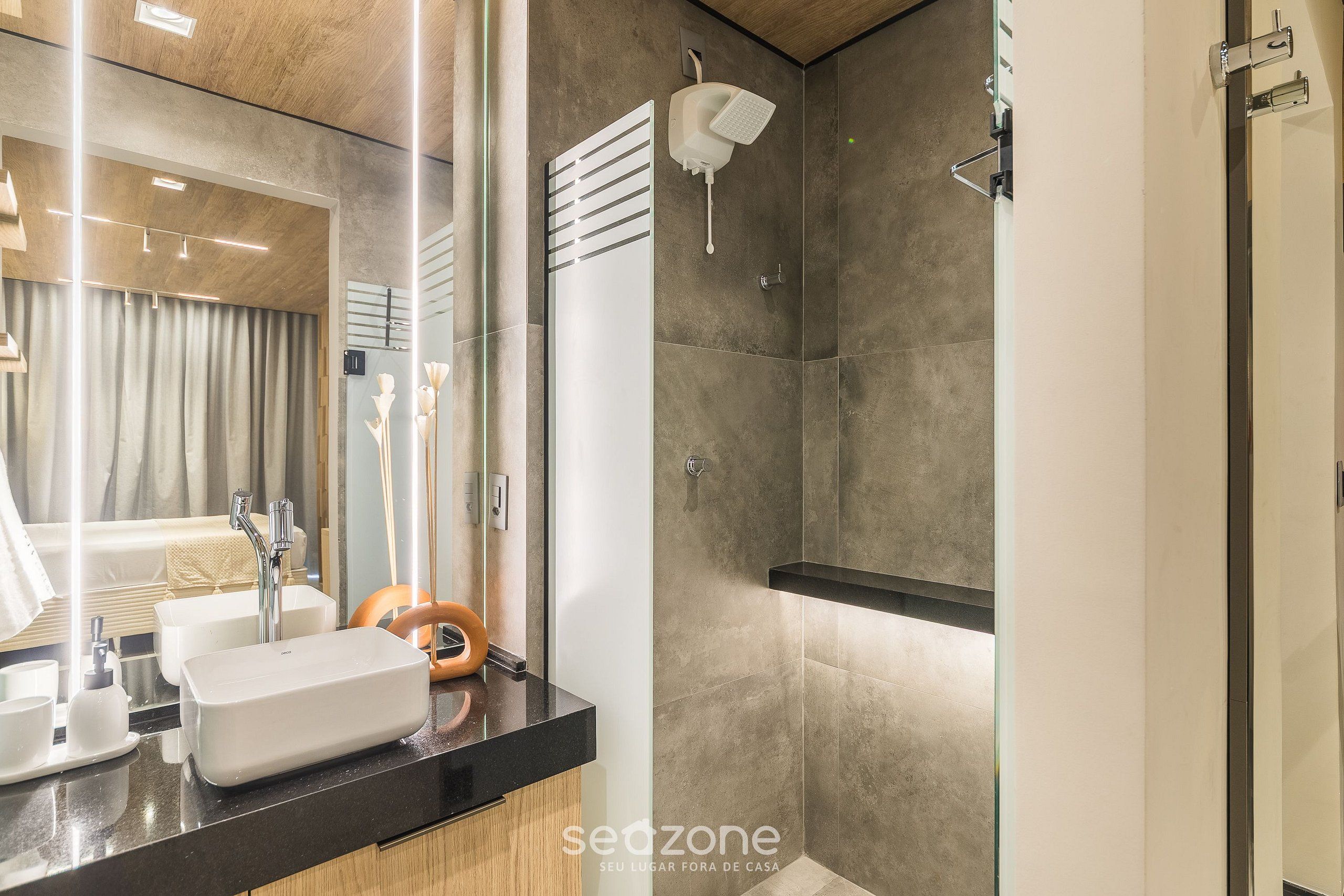 Un baño moderno con un espejo grande, un lavabo rectangular, un cabezal de ducha de mano y un box de ducha.