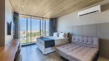 Un dormitorio moderno con una cama grande, un sofá, un televisor y vistas a la ciudad.