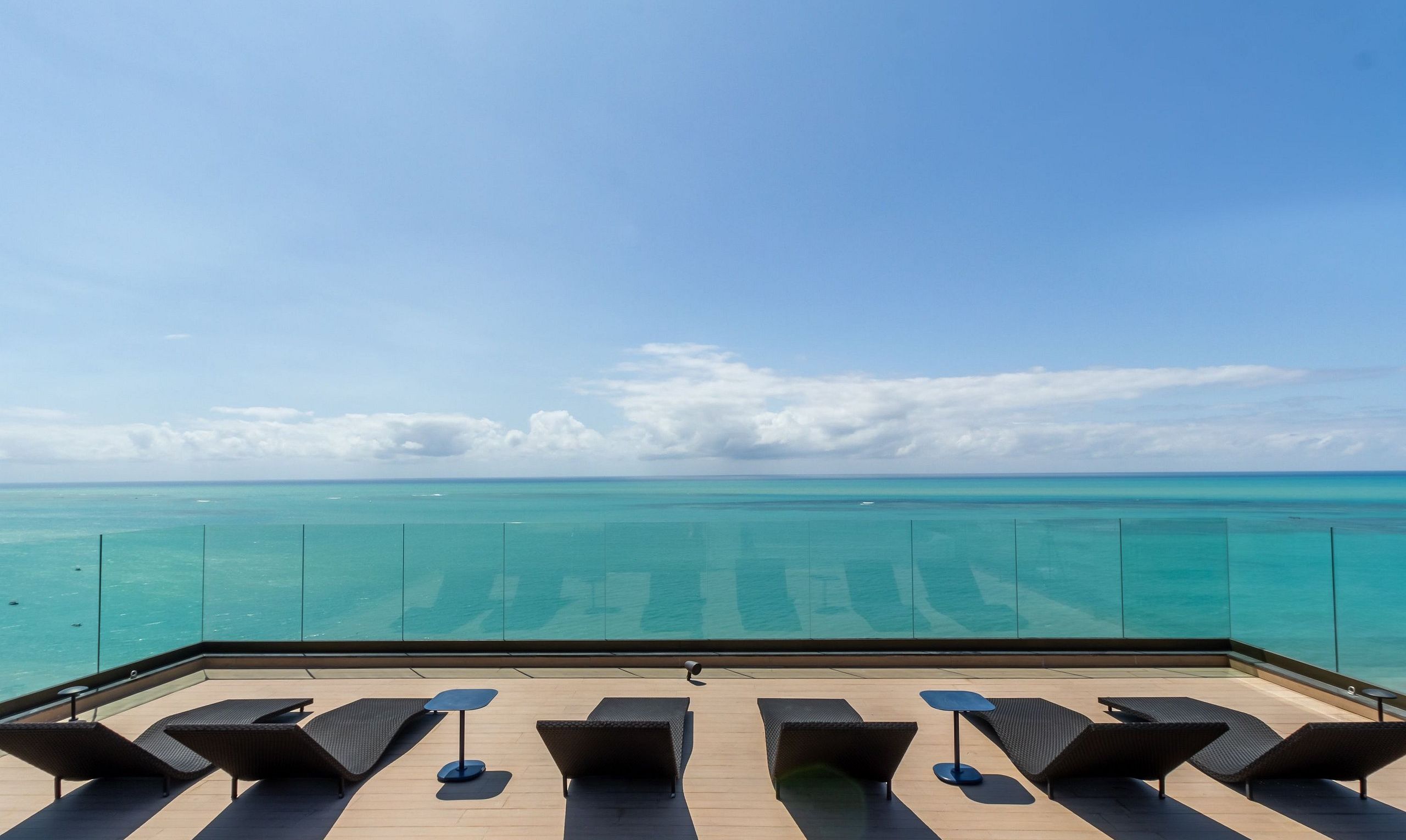 A rooftop terrace with lounge chairs and a view of the ocean.