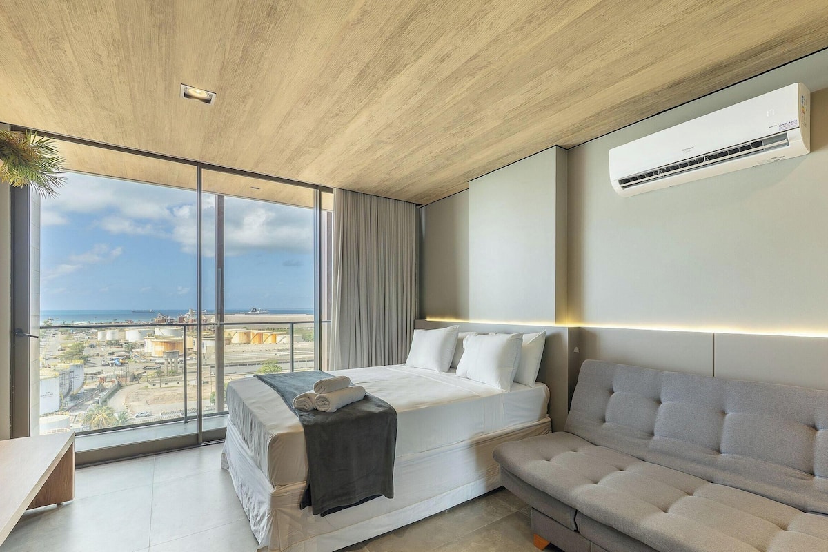 A modern hotel room with a large bed, a sofa, and a view of the cityscape.