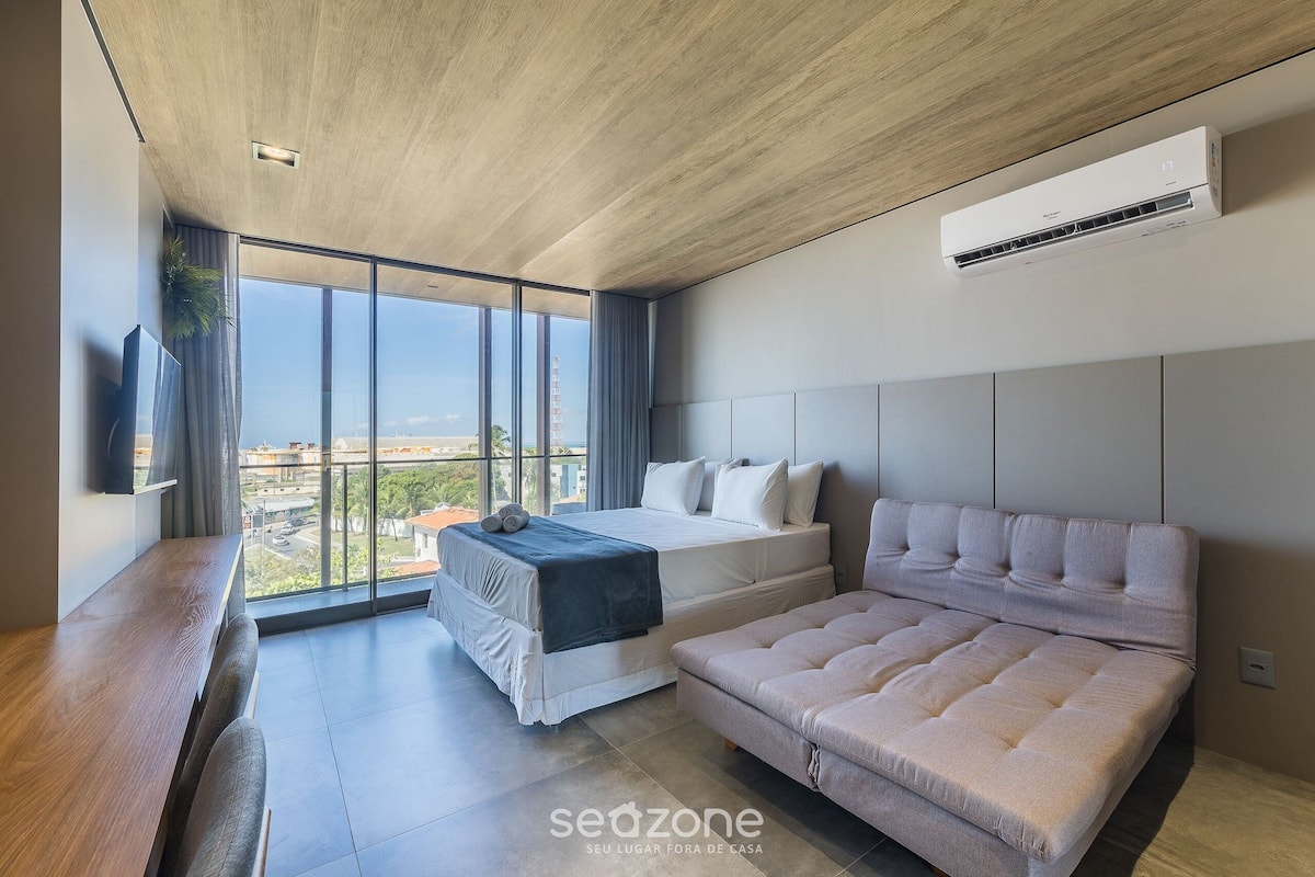 A modern bedroom with a large bed, a sofa, a TV, and a view of the city.