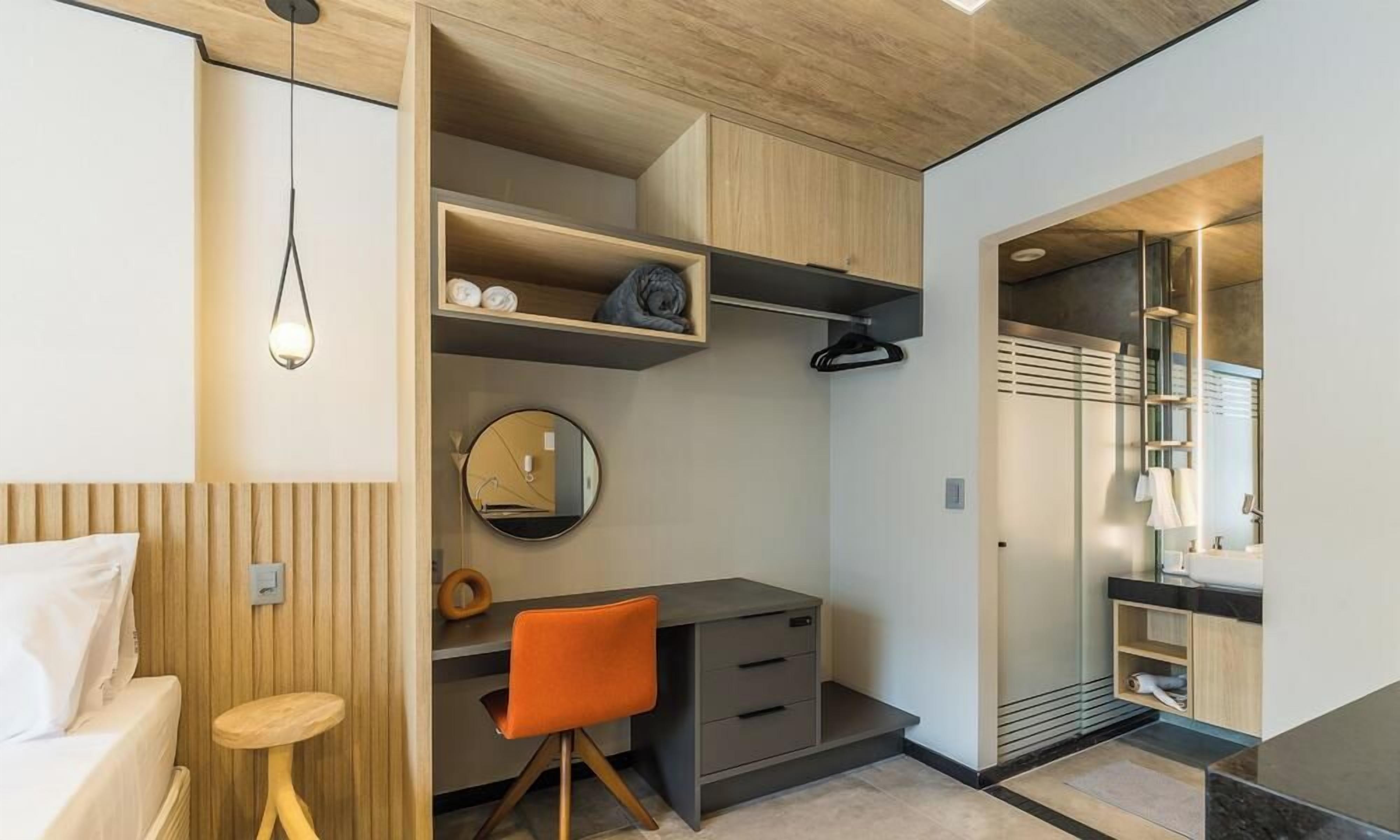 A compact bedroom with a bed, a desk, and a chair, a bedside table, and a wardrobe.