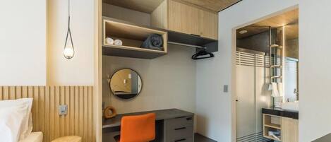 A compact bedroom with a bed, a desk, and a chair, a bedside table, and a wardrobe.