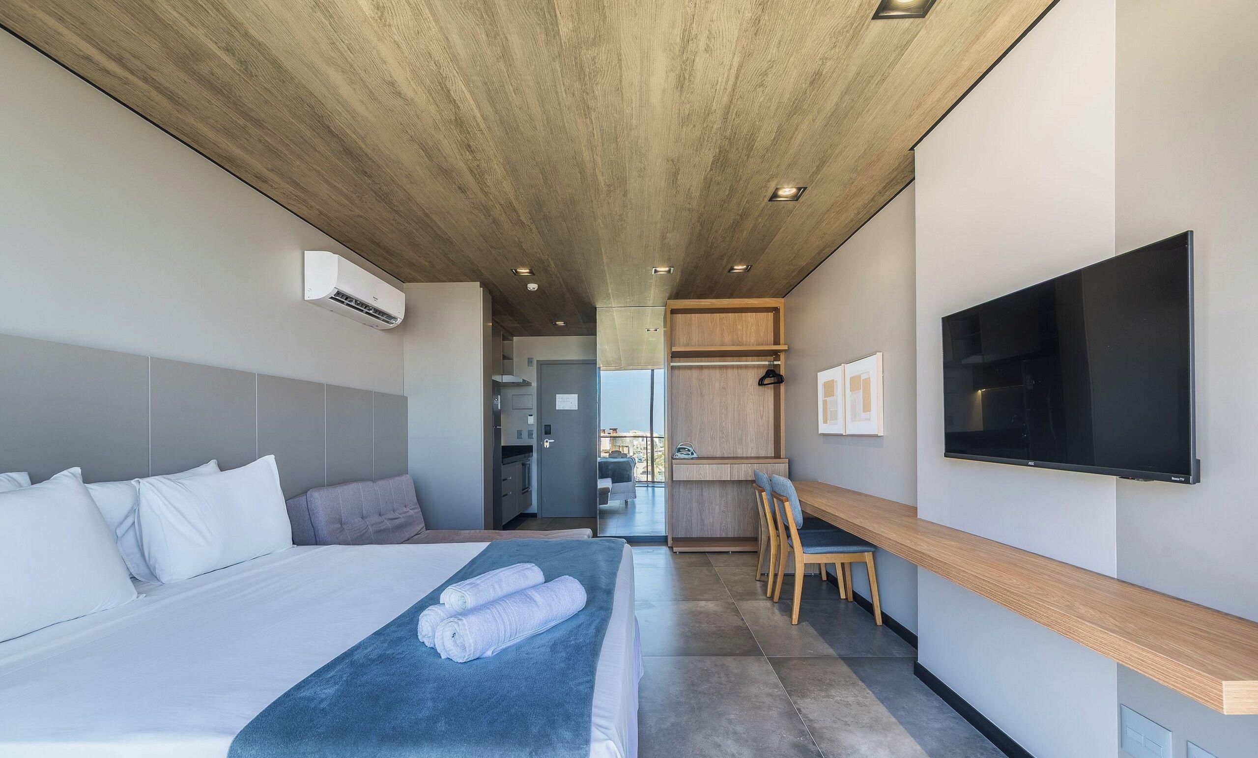 A modern hotel room with a bed, a desk, a flat-screen TV, and a view of the city.
