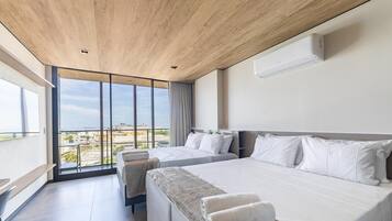 Una habitación de hotel moderna con una cama grande, una cama más pequeña y un sofá. Hay una ventana amplia con vista a la ciudad y al mar.